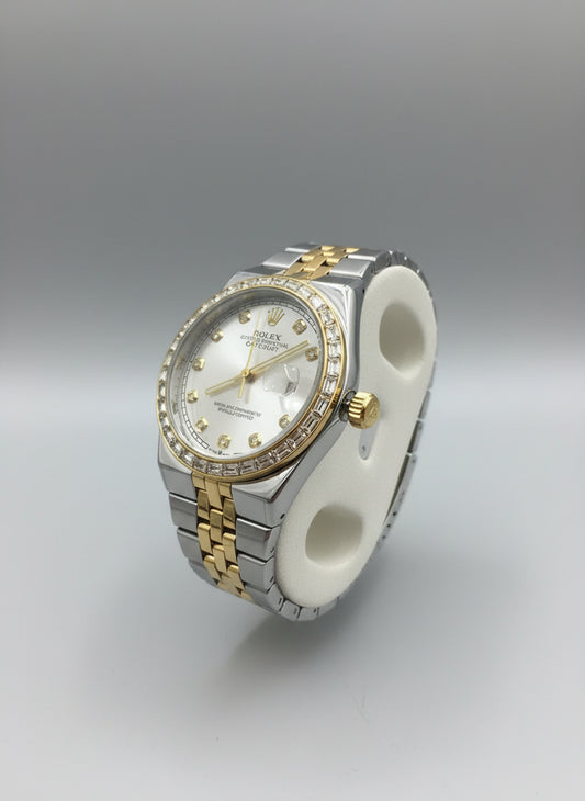 Two-tone watch with diamond accents on a white stand against a blurred background